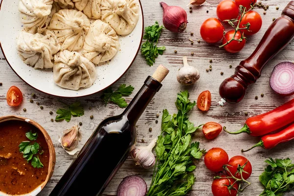 Vue de dessus de délicieux khinkali près de la bouteille de vin, kharcho, légumes et épices sur table en bois — Photo de stock