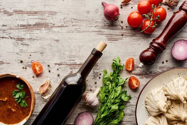 Top view of delicious khinkali near bottle of wine, kharcho, vegetables and spices on wooden table — Stock Photo