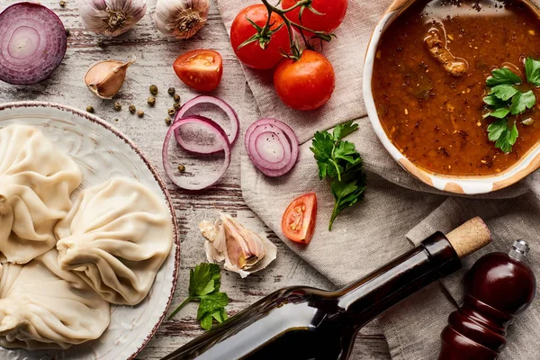 Vista superior del delicioso khinkali cerca de la botella de vino, kharcho, verduras y especias en la mesa de madera - foto de stock