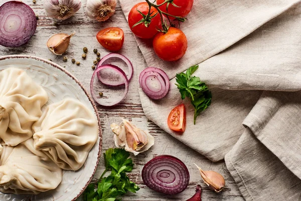 Vue du dessus de délicieux khinkali près des légumes, des épices et de la serviette sur table en bois — Photo de stock