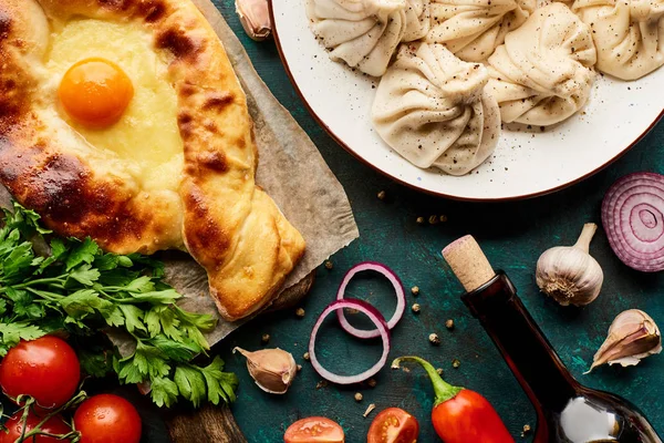 Vista superior de delicioso khinkali, Adjarian khachapuri y vino sobre fondo verde - foto de stock