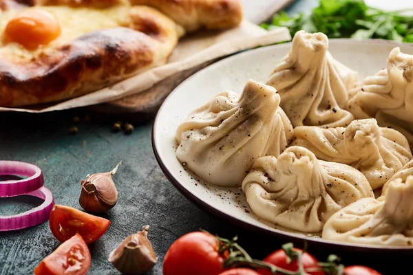 Close up view of delicious khinkali, Adjarian khachapuri and vegetables on green table — Stock Photo