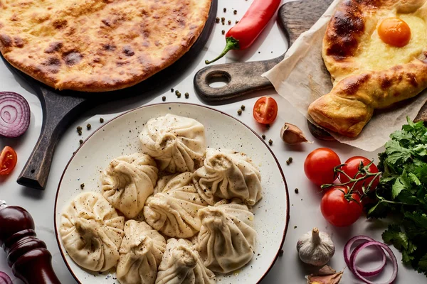 Blick von oben auf köstliches Chinkali und Chatschapuri in der Nähe von Gemüse und Gewürzen auf Marmortisch — Stockfoto