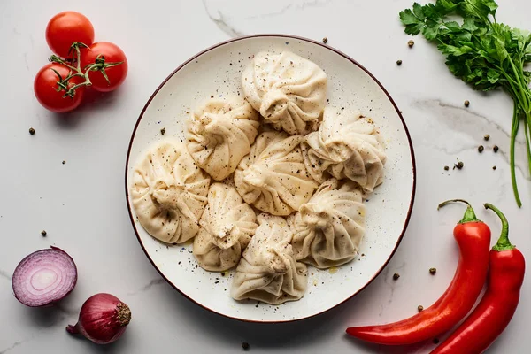 Blick von oben auf köstliches Chinkali in der Nähe von Gemüse und Gewürzen auf Marmortisch — Stockfoto