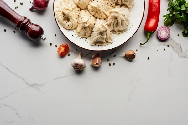 Blick von oben auf köstliches Chinkali in der Nähe von Gemüse und Gewürzen auf Marmortisch — Stockfoto