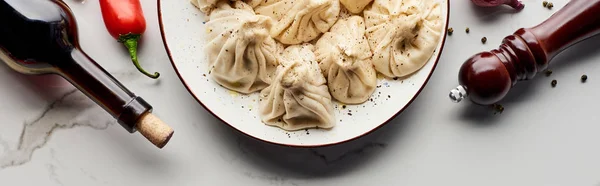 Top view of delicious khinkali near bottle of wine, vegetables and spices on marble table, panoramic shot — Stock Photo