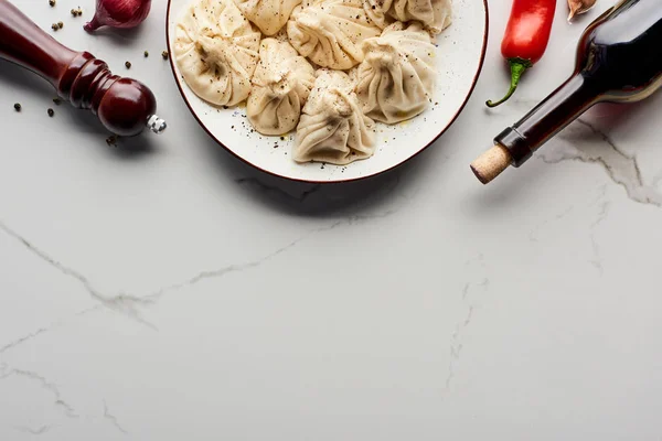 Blick von oben auf köstliches Chinkali in der Nähe einer Flasche Wein, Gemüse und Gewürzen auf einem Marmortisch — Stockfoto