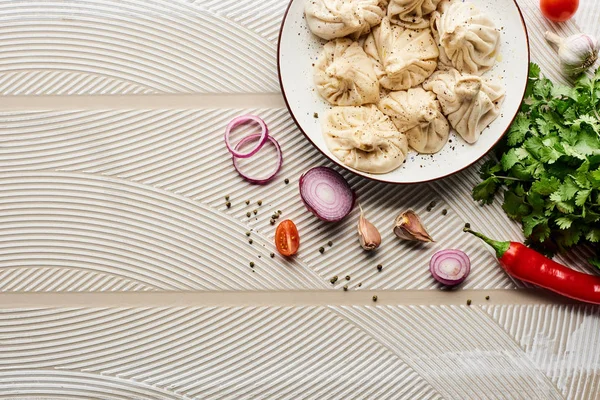 Vista dall'alto di deliziosi khinkali vicino a verdure e spezie su sfondo beige testurizzato — Foto stock