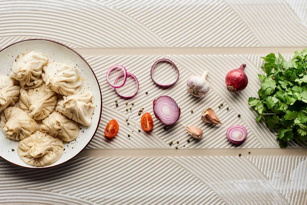 Vue du dessus de délicieux khinkali près des légumes et des épices sur fond texturé beige — Photo de stock