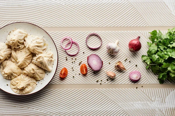 Vista superior de delicioso khinkali cerca de verduras y especias sobre fondo texturizado beige - foto de stock