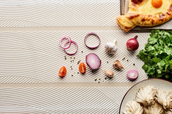 Vue du dessus de délicieux khinkali et adjarian khachapuri près des légumes et des épices sur fond texturé beige — Photo de stock