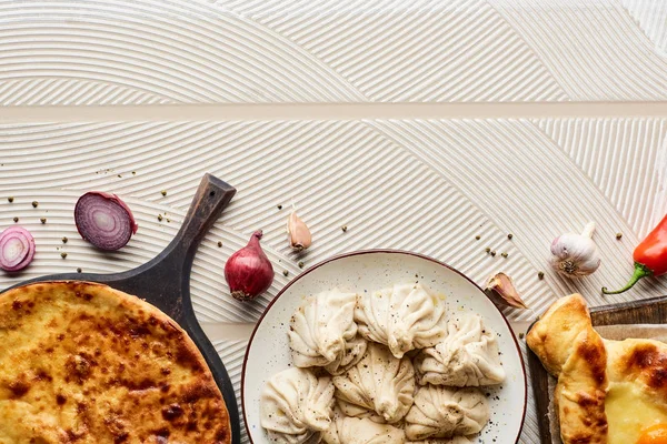 Vue du dessus de délicieux khinkali et khachapuri près des légumes et des épices sur fond texturé beige — Photo de stock