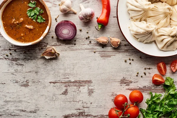 Vista superior de khinkali delicioso, kharcho perto de legumes e especiarias na mesa de madeira — Fotografia de Stock