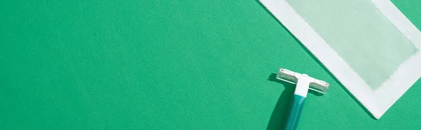 Top view of green disposable razor and depilation wax stripe on green background, panoramic shot — Stock Photo