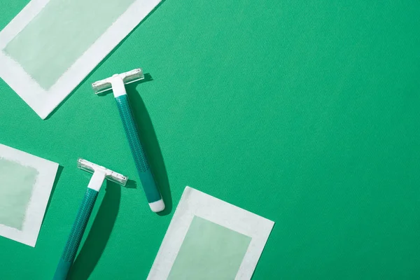 Top view of green disposable razors and depilation wax stripes on green background — Stock Photo