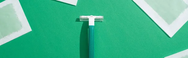 Top view of green disposable razor and depilation wax stripes on green background, panoramic shot — Stock Photo