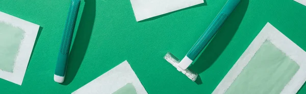 Vista superior de maquinillas de afeitar desechables verdes y rayas de cera depilación sobre fondo verde, plano panorámico - foto de stock