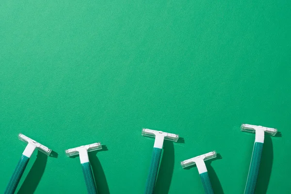 Vista superior de maquinillas de afeitar desechables verdes sobre fondo verde - foto de stock