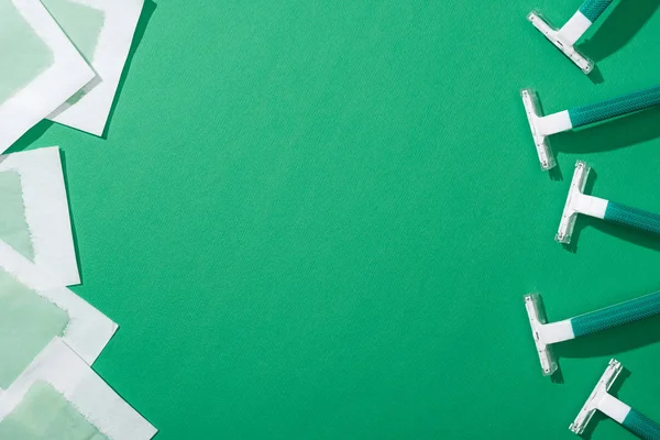 Top view of green disposable razors and depilation wax stripes on green background with copy space — Stock Photo