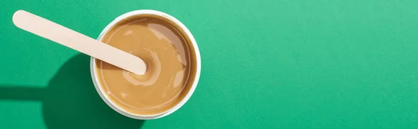 Top view of depilation wax in cup with stick on green background, panoramic shot — Stock Photo