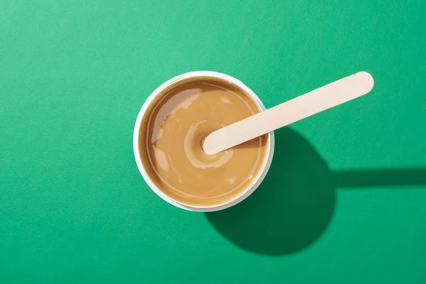 Vista superior de la cera de depilación en taza con palo sobre fondo verde - foto de stock