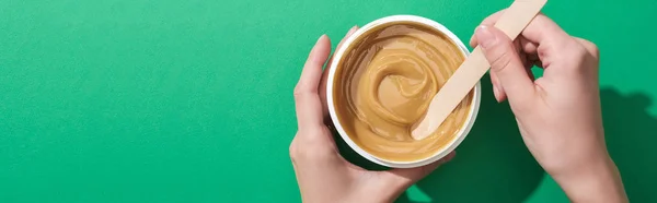 Vista recortada de la mujer sosteniendo palo y taza con cera depilación sobre fondo verde, tiro panorámico - foto de stock