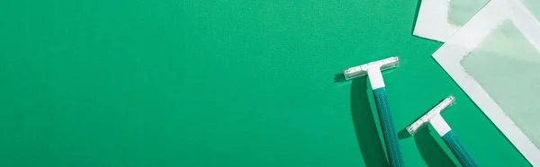 Top view of green disposable razors and depilation wax stripes on green background with copy space, panoramic shot — Stock Photo