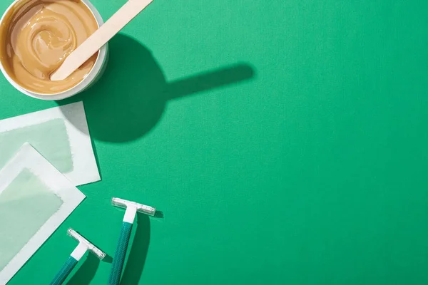 Top view of green disposable razors, wax and depilation stripes on green background — Stock Photo