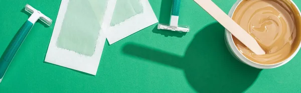 Top view of green disposable razors, wax and depilation stripes on green background, panoramic shot — Stock Photo