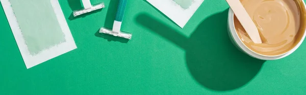 Top view of green disposable razors, wax and depilation stripes on green background — Stock Photo