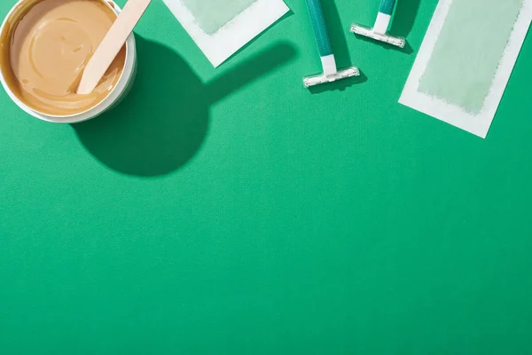 Top view of green disposable razors, wax and depilation stripes on green background — Stock Photo