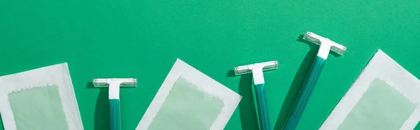 Top view of green disposable razors and depilation wax stripes on green background, panoramic shot — Stock Photo