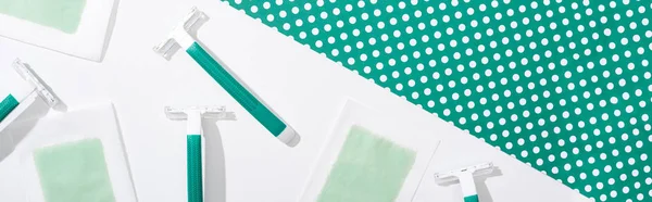 Top view of green disposable razors and depilation wax stripes on green and white dotted background, panoramic shot — Stock Photo