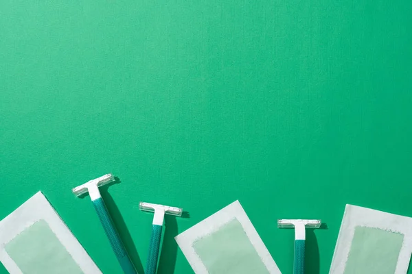 Top view of green disposable razors and depilation wax stripes on green background with copy space — Stock Photo