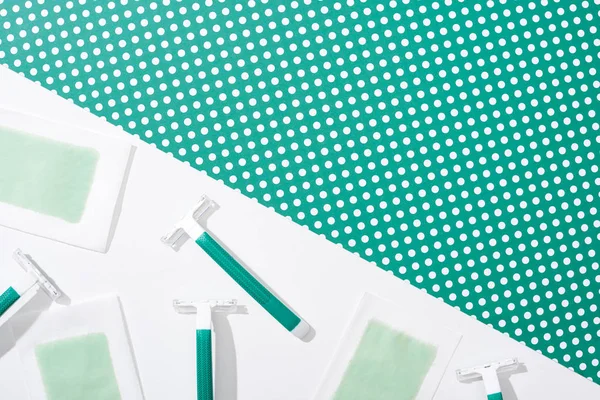 Vue de dessus des rasoirs jetables verts et des rayures de cire d'épilation sur fond vert et blanc pointillé — Photo de stock