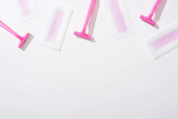 Vista superior de maquinillas de afeitar de color rosa y rayas de cera depilación sobre fondo blanco - foto de stock