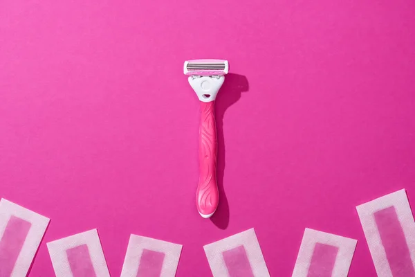 Vista dall'alto di rasoio femminile e depilazione strisce di cera su sfondo rosa — Foto stock