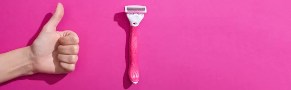Vista recortada de la mujer que muestra el pulgar hacia arriba cerca de la navaja de afeitar sobre fondo rosa, plano panorámico - foto de stock