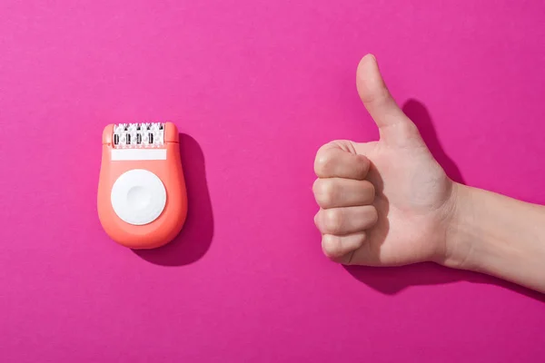 Vista ritagliata della donna che mostra pollice verso l'alto vicino epilator su sfondo rosa — Foto stock