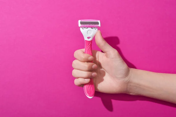 Recortado vista de la mujer sosteniendo la navaja de afeitar sobre fondo rosa - foto de stock