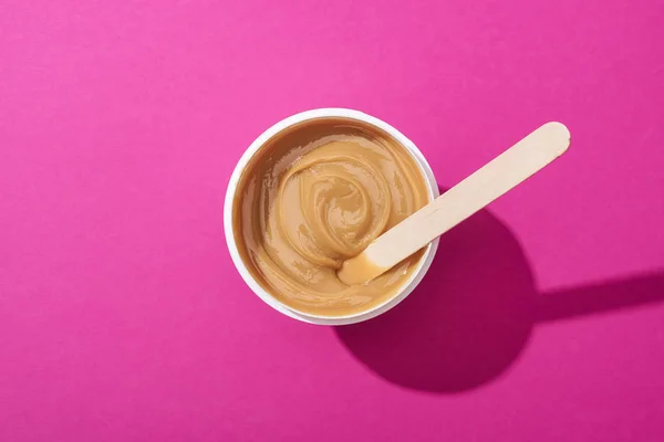 Vista superior de la depilación de cera en taza con palo sobre fondo rosa - foto de stock