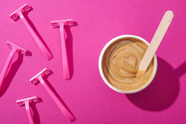 Top view of disposable razors and depilation wax in cup with stick on pink background — Stock Photo