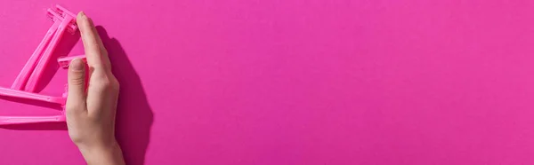 Vue recadrée de la main près de rasoirs jetables sur fond rose, vue panoramique — Photo de stock