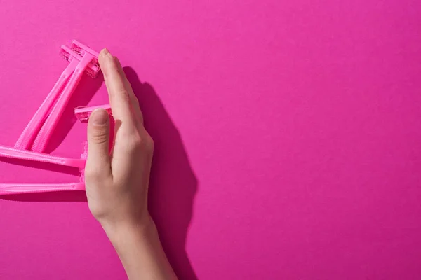 Vista recortada de la mano cerca de máquinas de afeitar desechables sobre fondo rosa - foto de stock