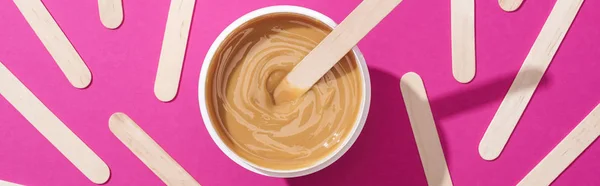 Top view of depilation wax in container with sticks on pink background, panoramic shot — Stock Photo