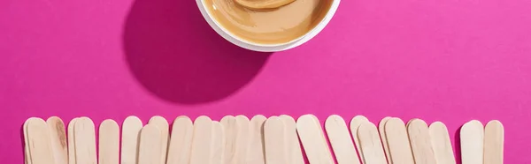 Top view of depilation wax in container with sticks on pink background, panoramic shot — Stock Photo