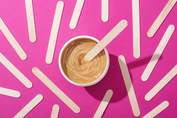 Top view of depilation wax in container with sticks on pink background — Stock Photo