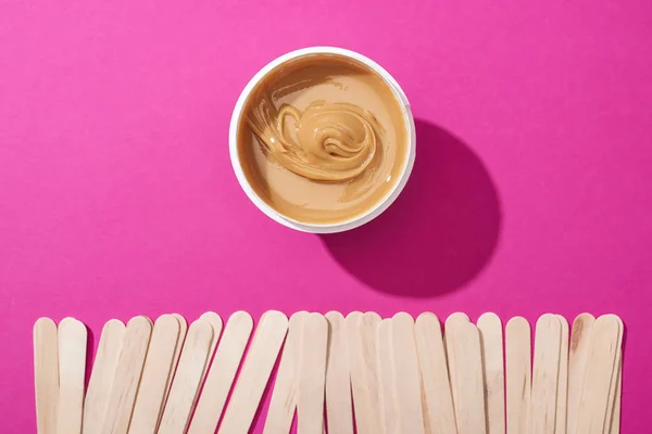 Top view of depilation wax in container near sticks on pink background — Stock Photo