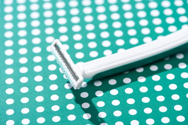 Vista de cerca de afeitadora desechable sobre fondo punteado verde y blanco - foto de stock