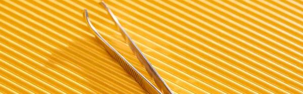 Pinzas de acero inoxidable sobre fondo texturizado amarillo, plano panorámico - foto de stock